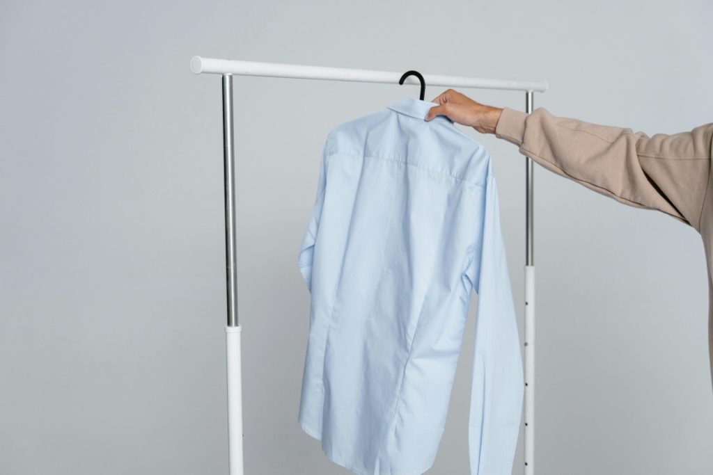 A person holding a blue shirt on a rack against a neutral background.